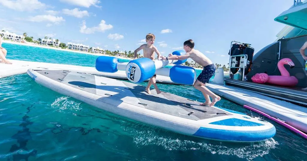 Two male children holding inflatable FunAir Water Joust Poles stood on a SUP